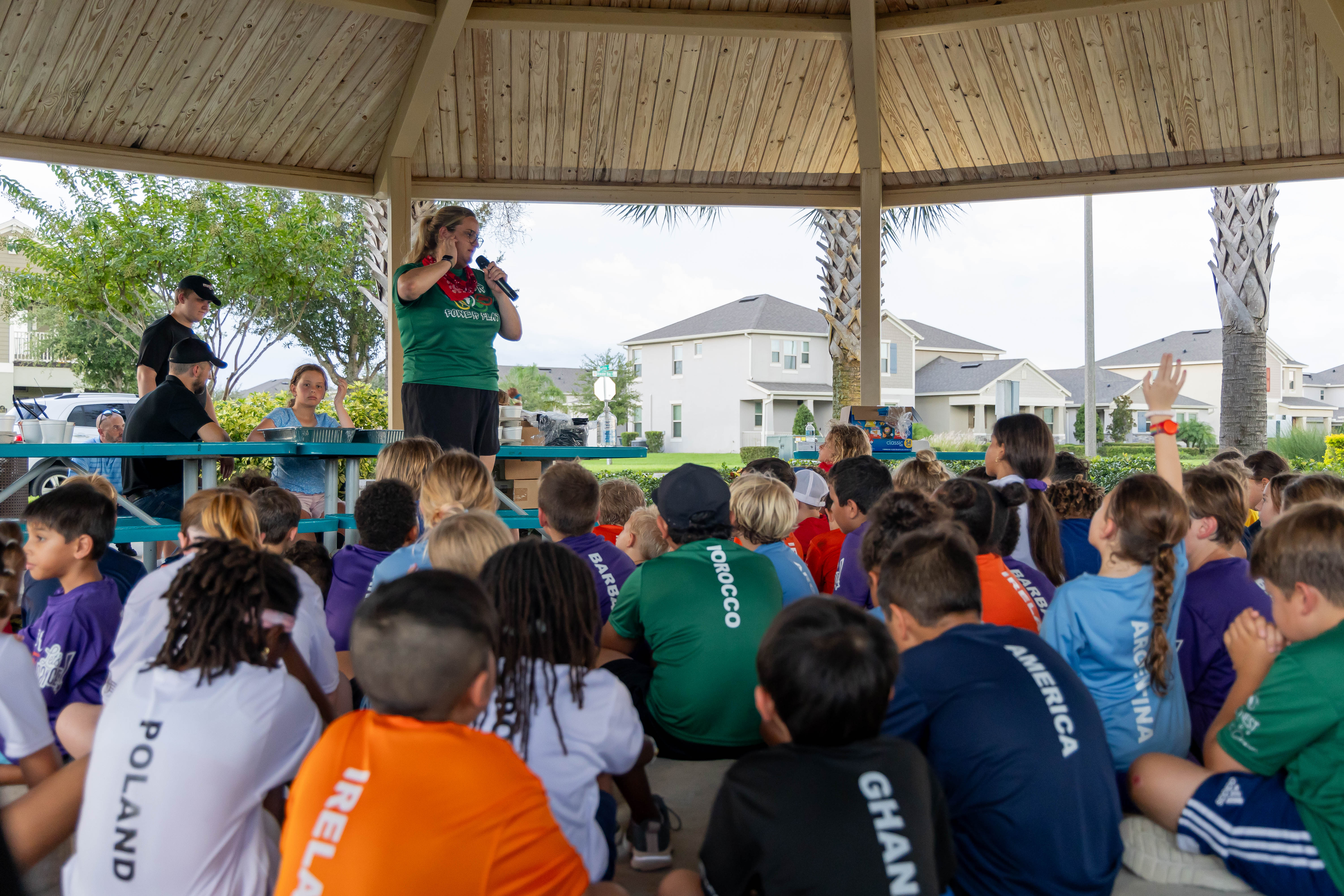 Coach speaking to campers wearing country-team jerseys at the gazebo